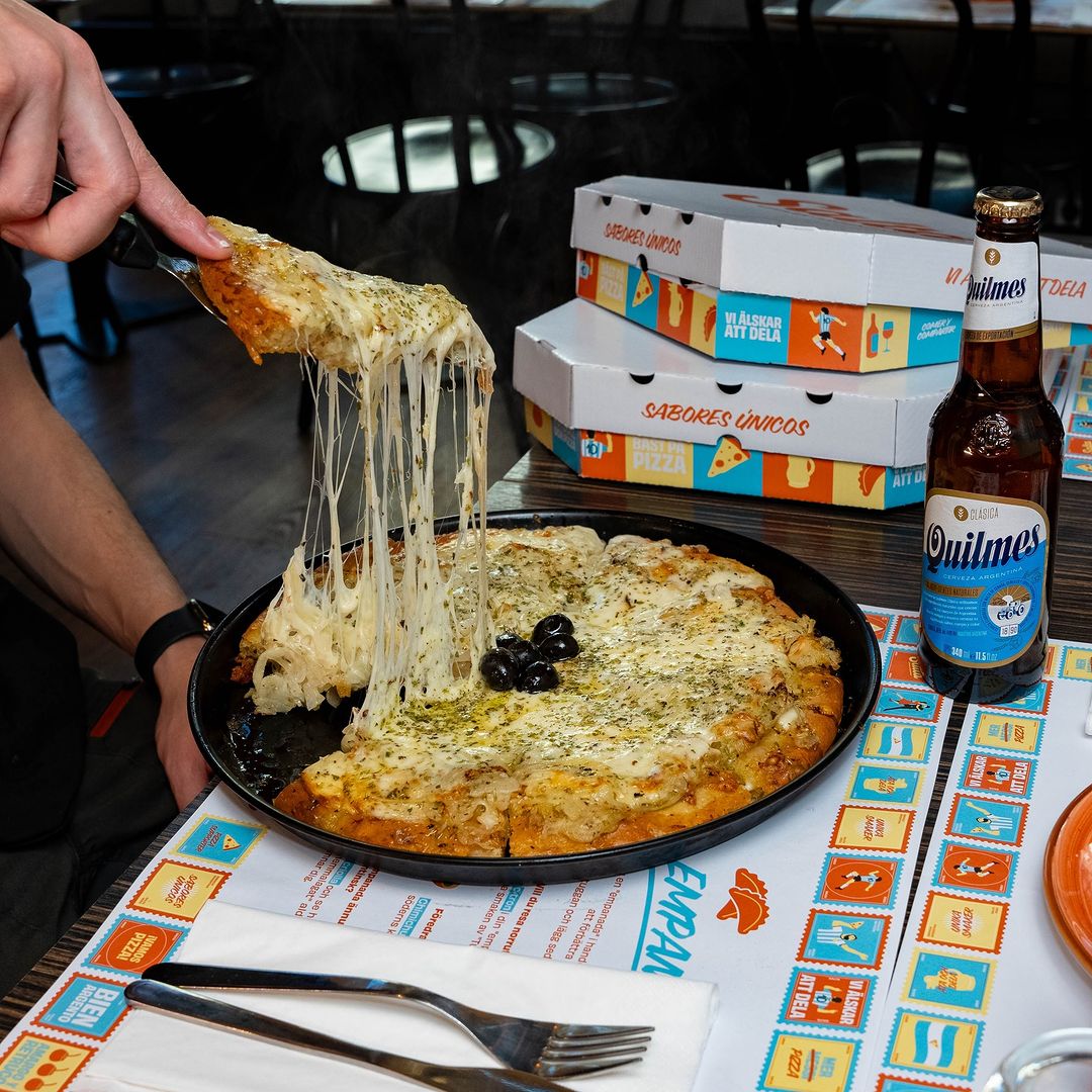 Cheesy pizza in focus with personalized pizza boxes displayed in the background.